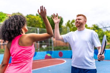 Çok ırklı kadın ve erkek takımı, Pickleball oynarken kutlama yaparken beşlik çakıyor.