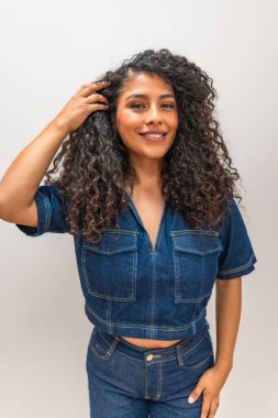 Güzel kıvırcık saçlarına dokunan Latin bir kadının dikey üç çeyrek boy portresi.