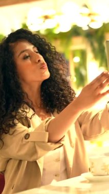 Kafeteryada selfie çeken kendine güvenen Latin bir kadının dikey portresi.