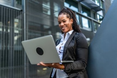 Modern bir binanın önünde dizüstü bilgisayarla çalışan kendine güvenen İspanyol iş kadını.
