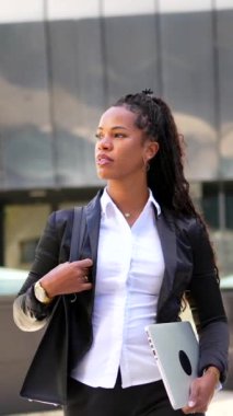 Şehirde modern bir binanın yanında dizüstü bilgisayar taşıyan Latin bir iş kadınının portresi.