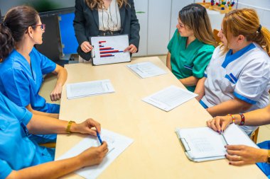 Toplantı odasında oturan hemşirelere ve sağlık çalışanlarına grafikler ve veriler gösteren yaşlı bir müdür.