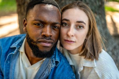 Çok ırklı bir çiftin parkta yanak yanağa yakın görüntüsü.