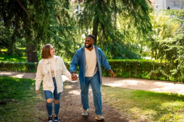 Parkta el ele tutuşan, sıradan kıyafetler giyen, çok ırklı mutlu bir çift.