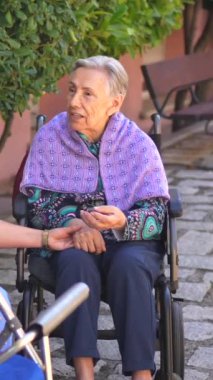 Kadın hemşire ve yaşlı kadın huzurevinin bahçesinde konuşuyor ve dinleniyorlar.