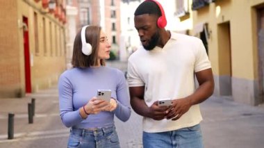 Cep telefonu kullanan ve sokakta müzik dinleyen çok ırklı bir çift.