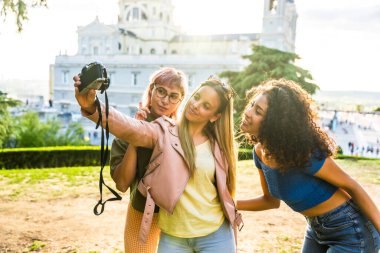 Kadın arkadaşlar gün batımında şehrin görüş açısında dijital kamerayla selfie çekiyorlar.