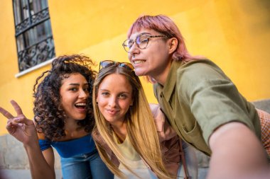 Diverse young women gesturing success while taking selfie together in the city clipart