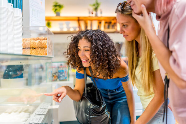 Happy friends buying ice cream in a shopping mall pointing to the glass counter choosing the flavor