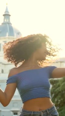 Şehir manzarasında gün batımına karşı parkta dans eden özgür Latin kadın.