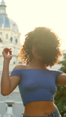 Güzel, Latin, şehvetli ve mutlu bir kadın günbatımına karşı arka planda kiliseyle dans ediyor.