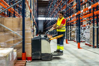Güvenli giysiler içinde bir depoda forklift kullanarak paletleri taşıyan bir adam.