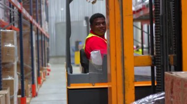Bir dağıtım deposunda forklift kullanırken gülümseyen Latin işçiler.