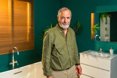 Evde, banyoda kameraya gülümseyen beyaz bir adamın portresi.