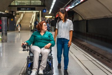 Kafkas engelli mutlu bir kadın ve metro platformu boyunca yürüyen çok ırklı bir arkadaşın önden görünüşü