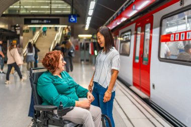 Tekerlekli sandalyedeki engelli kadın ve metro istasyonunda beklerken konuşan arkadaşı.