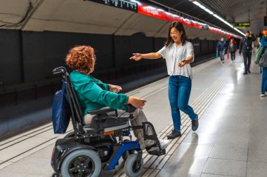 Çinli mutlu kadın, metro istasyonunda tekerlekli sandalyedeki engelli arkadaşını kucaklamaya geliyor.