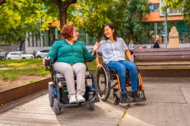 Şehir parkında konuşan, çok ırklı, neşeli, engelli iki kadın.