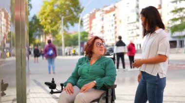 Engelli bir kadın ve Asyalı bir bakıcı şehirde rahat rahat konuşuyor.