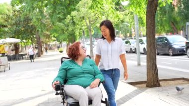 Elektrikli sandalye kullanan engelli bir kadın ve şehirde yürürken konuşan Çinli bir arkadaş.