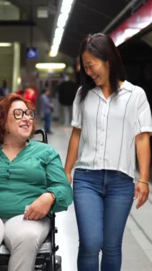 Kafkas engelli mutlu bir kadın ve metro platformu boyunca yürüyen çok ırklı bir arkadaşın önden görünüşü