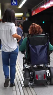 Engelli bir kadının arka görünüşü ve metro peronundaki bakıcı.