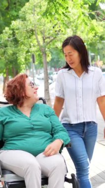 Elektrikli sandalye kullanan engelli bir kadın ve şehirde yürürken konuşan Çinli bir arkadaş.