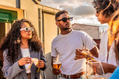 Multi-ethnic modern friends talking in a rooftop while drinking wine and eating snacks clipart