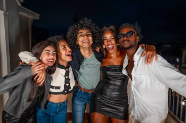 Çok ırklı erkek ve kadın arkadaş grubunun portresi. Geceleri omuzlarından sarılıyorlar ve parti yapıyorlar.