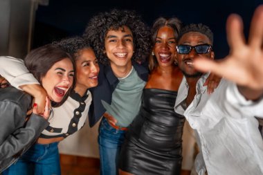 Mutlu çoklu etnik arkadaşlar şakalaşırken arkadan sarılıyorlar ve bir gece partisinde gülümsüyorlar.