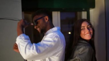 Geceleri çatıdaki bir partide Latin bir kadınla arka arkaya dans eden afro bir adam.