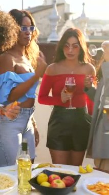 Çok ırklı insanlar çatıda akşam partisini kutluyor şarap içiyor ve sohbet ediyorlar.