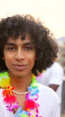 Çatı katında parti yaparken gülümseyen kıvırcık saçlı ve Hawaii kolyeli mutlu bir adam.