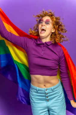 Elinde lgbt gökkuşağı bayrağı olan mutlu bir kadının mor arkaplanlı stüdyo portresi