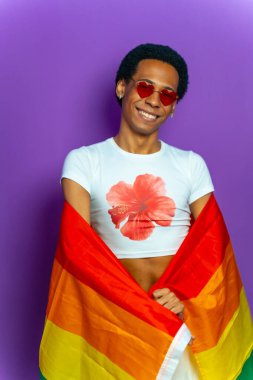 Lgbt bayrağıyla sarılmış mor bir transseksüel latin adamın kamera önünde gülümseyen portresi.