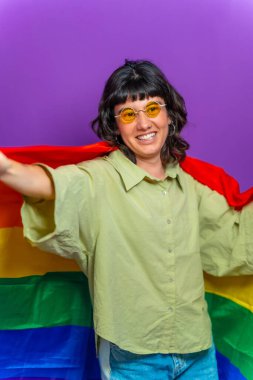 İkili olmayan mutlu birinin mor arkaplanlı stüdyo portresi lgbt gökkuşağı bayrağını göndere çekiyor