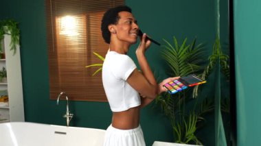 Evde banyo aynasına bakarak makyaj yapan eşcinsel latin adam.