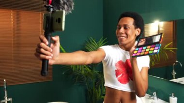Makyaj dersini kaydederken cep telefonu kullanan mutlu Latin gay adam.