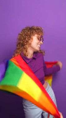Elinde lgbt gökkuşağı bayrağı olan mutlu bir kadının mor arkaplanlı stüdyo portresi