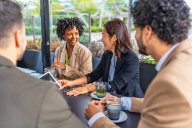 Modern bir kafeteryadaki toplantı sırasında dijital tablet kullanan iş adamları
