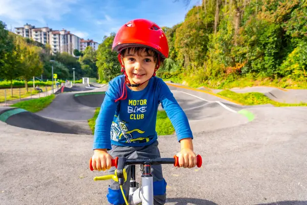 Genç bir çocuk kask takmış bisiklet sürüyor. Gülümsüyor ve eğleniyor.