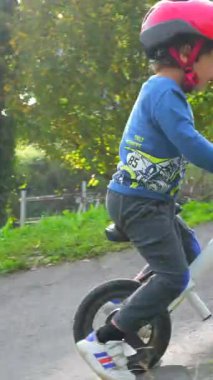 Genç bir çocuk tepeden aşağı bisiklet sürüyor. Çocuk bir kask ve mavi bir gömlek giyiyor. Sahne açık havada ve çocuk gezintiden zevk alıyor.