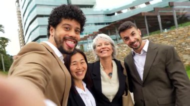 Bir grup iş adamı, tropik bir şehirde finans binasının önünde selfie çekiyor.