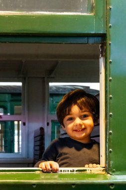 Genç bir çocuk tren penceresinden kameraya gülümsüyor.
