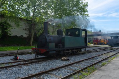 Bir tren rayların üzerinde oturuyor ve içinden duman çıkıyor. Tren eski ve siyah bir motoru var.