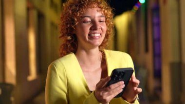 Casual beauty woman with curly hair expressing surprise while using smartphone in the city at night