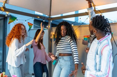 Afrikalı bir kadın dans ederken, çok ırklı arkadaşlar onu çatı partisinde çevreledi.