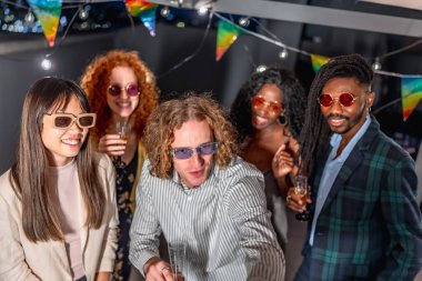 Şık elbiseli ve güneş gözlüklü çeşitli arkadaşlar birlikte selfie çekiyorlar terasta bir gece partisinde şampanya içiyorlar