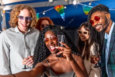 Çok ırklı şık arkadaşlar gece eğleniyorlar ve şampanya kadehlerini kaldırırken selfie çekiyorlar.