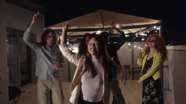 Çinli stil sahibi genç bir kadın gece partisinde çok ırklı arkadaşlarıyla dans etmekten zevk alıyor.